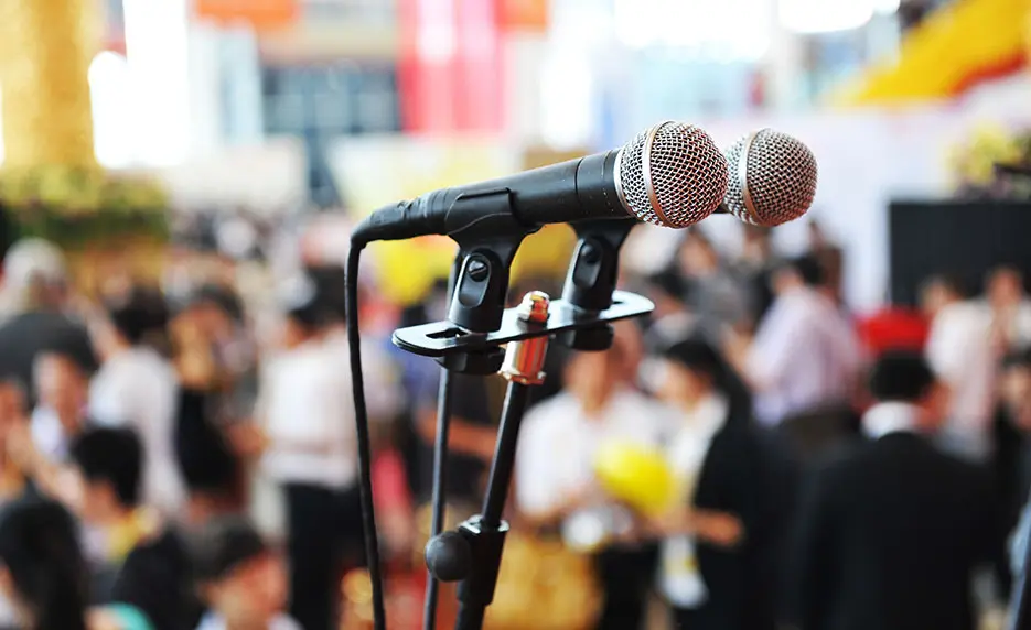 A photo of two microphones in front of a blurred audience.